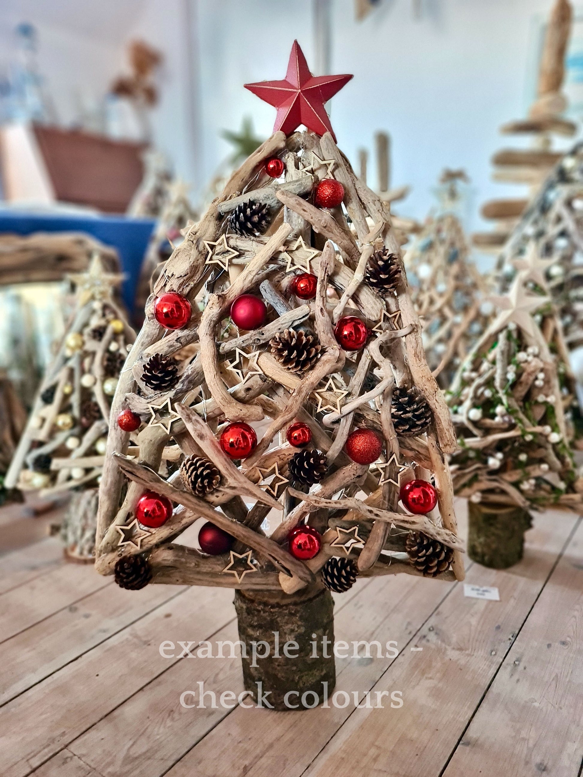 Decorative Christmas tree made of driftwood with red ornaments and a star on top, placed on a wooden surface.