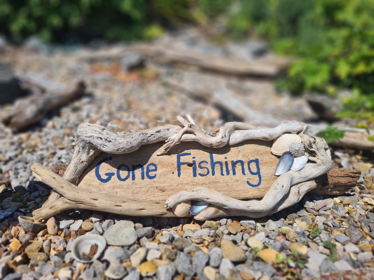 driftwood log with "gone fishing" painted on and decorated with shells